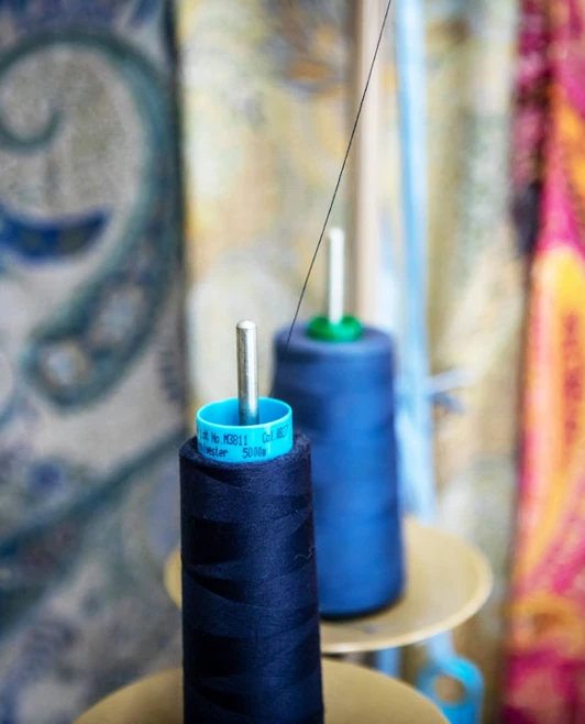 Close-up of navy blue thread spools with colorful fabric in the background in the fashion design studio. Close-up of navy blue thread spools with colorful fabric in the background in the fashion design studio.